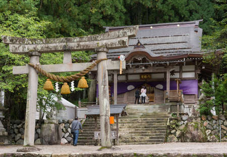 Takayama, Japan - September 23, 2016: The small gray-brown Shirakawahachiman Shrine in Takayama is up a stairway. A few people present. Green foliage and a stone Toriiのeditorial素材
