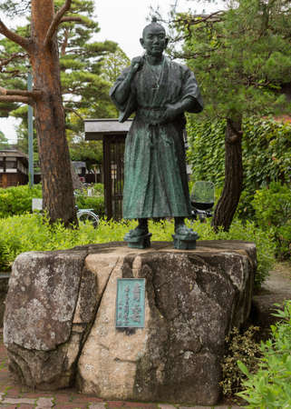 Takayama, Japan - September 24, 2016: Life-size, greening bronze statue of young Samurai in traditional outfit standing on rock. Trees and green foliage around. Title is Blue Cloud. Honors youth.のeditorial素材
