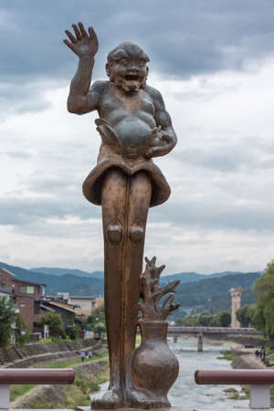 Takayama, Japan - September 24, 2016: Statue of Ashinaga Zuchi Zou on Miyazawa River Kaji bridge. He is a character in folk tale. Shot against cloudy sky. View of river, mountains, buildings.のeditorial素材