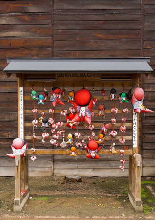 Takayama, Japan - September 24, 2016: Wooden rack of Sarubobo folk deity in different colors at Hikakokubun-ji Buddhist Temple. Idol is good luck charm. Also called Monkey Child. Dark wooden background.のeditorial素材