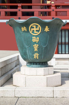 Tokyo, Japan - September 26, 2016: In front of vermilion Honzo main hall of the Senso-ji Buddhist Temple, stands a sculpture of a giant vase painted dark green. Gold swastika and Japanese characters.のeditorial素材