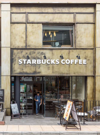 Tokyo, Japan - September 28, 2016: Smaller two-level Starbucks coffee shop in Minamiaoyama neighborhood. Brown-beige facade, signs, clients, outdoor patioのeditorial素材