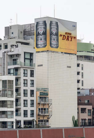 Tokyo, Japan - September 28, 2016: An Asahi Super Dry lager beer can billboard on top of some older apartment buildings along the Sumida River. Mostly white buildings, gray sky. Beer Sign adds the color.のeditorial素材