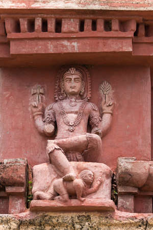 Dindigul, India - October 23, 2013: On top of Vimanam at the abandoned ruinous Shiva Temple on the Rock in Dindigul. Red painted sandstone features relatively well saved statue of sitting Shiva with foot on the dwarf, ignorance.のeditorial素材
