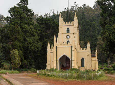 Ooty, India - October 25, 2013: The yellow painted castle-like Saint Stevens Church in Ooty. Red dirt and rose garden with dark green foliage in background.のeditorial素材