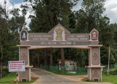 Ooty, India - October 25, 2013: The man rectangular gate over road into Wellington Cantonment. Features names and logos of garrison and college. Green foliage in back. Guard on duty.のeditorial素材