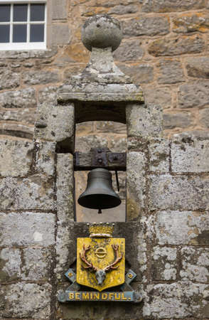 Cowdor, Scotland - June 2, 2012: The black bell hangs in gray stone niche above the golden coat of arms and slogan, Be Mindful. In the arch above the entrance gate to the courtyard of historic Cowdor Castle.のeditorial素材