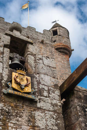 Cowdor, Scotland - June 2, 2012: The brown-gray stone structure of main gate of undamaged Cowdor Castle. Flag on top. Golden emblem with slogan. Guard tower.のeditorial素材