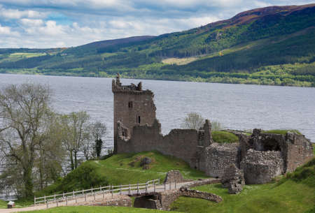 Loch Ness, Scotland - June 2, 2012: The ruins of  Urquhart Castle sit on a green cliff looking over  Loch Ness. Surrounding green hills. Light blue sky with white clouds.のeditorial素材