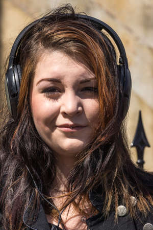 Inverness, Scotland - June 1, 2012: Portrait of head of young woman with dark and red hair. She wears black headphones and sports piercings in her lips. Serious looking.のeditorial素材