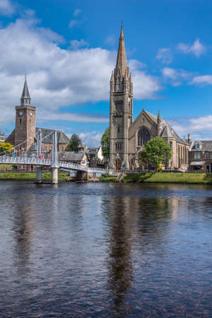 Inverness, Scotland - June 1, 2012: Combination photo of the Old High Church on the left and the Free Church of Scotland behind the Ness River with part of metallic Greig Street suspension bridge, under blue sky.のeditorial素材