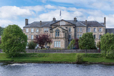 Inverness, Scotland - June 1, 2012: Main brown stone building of the University of Highlands and Islands, seen from across the Ness River. Flag on top. Green trees. Blue sky with white clouds.のeditorial素材