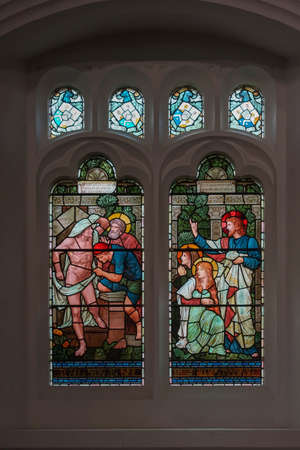 Grasmere, England - May 30, 2012: Bright colored stained glass window at Saint Oswald Church shows scene out of Jesus life. Set in dark wall with smaller windows. Jesus tells to release a naked captive man.のeditorial素材