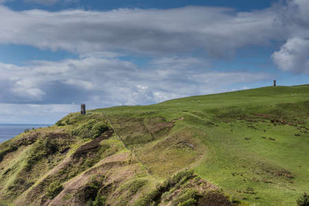 Berriedale, Scotland - June 4, 2012: Two medieval fire or light towers on top of the green cliffs as danger signs on the shoreline of the North Sea under blue sky with gray-white clouds.のeditorial素材