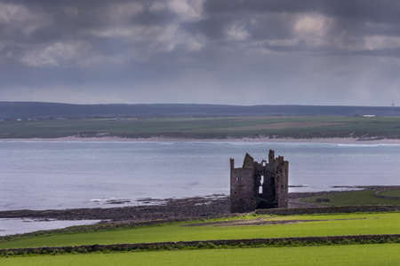 Nybster, Scotland - June 4, 2012: On the shore of a calm North Sea at the bay stands the ruin of the local strong house or castle under cloudy sky. Green meadows in front. Darker hills and beach on other side of bay.のeditorial素材