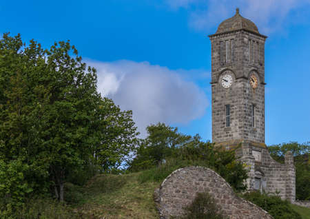 Helmsdale, Scotland - June 4, 2012: The Great War Memorial and gray stone Clock Tower stands on a hill just outside the town. Green vegetation and blue sky.のeditorial素材