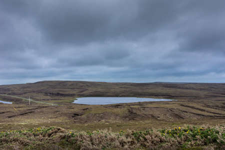 Lake in relative flat waste land behind Dunnet Head lighthouse. Cloudy gray-blue sky. Terrain is...
