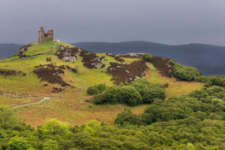 North Coast, Scotland - June 6, 2012: On a bright green hilltop stand the remains of a castle tower near the village of Tongue under a dark gray sky. Foreground is the hill with many hues of green and brown.のeditorial素材