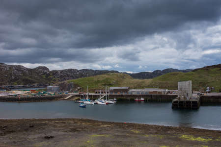 Northwest Coast, Scotland - June 6, 2012: The mid section of Scourie harbor shows the docks, a dozen yachts on the ocean water. Against gray rocky hills with green pasture patches. Heavy rain cloudscape.のeditorial素材