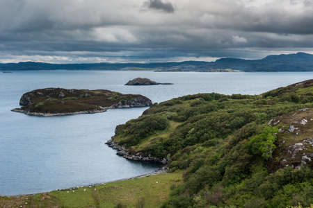 View from higher up Drumbeg hamlet onto Atlantic Ocean under dark cloudy sky. Rocky islands with...