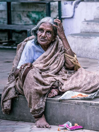 Madurai, India - October 19, 2013: An old graying lady sits on the sidewalk of the street around Meenakshi Temple. She has an expressive dismissing face, scratches her hair and wears a brownish sari.のeditorial素材