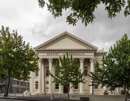 Auckland, New Zealand - March 1, 2017: Greek-Roman architecture for beige facade with triangular frieze of Baptist Tabernacle in Queen Street. Green vegetation and line of pillars.のeditorial素材