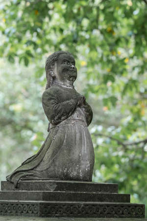 Auckland, New Zealand - March 1, 2017: Closeup of old stone statue, impacted by a century of weather, of praying girl with green vegetation in back at Symonds Street cemetery.のeditorial素材