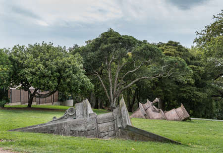 Auckland, New Zealand - March 1, 2017: Collection of statues in Western Park pretend to be pieces of stone facades half buried in the green lawn. Trees as background.のeditorial素材