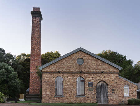 Auckland, New Zealand - March 2, 2017: Old brick pup station with tall chimney, now museum and theater, at lake Pupuke. Green vegetation under blue early morning sky.のeditorial素材