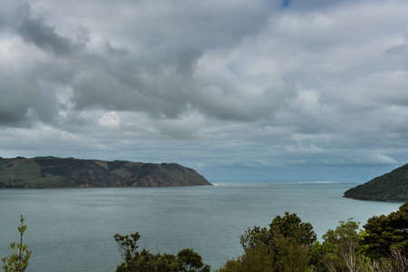 Auckland, New Zealand - March 2, 2017: Entrance from Tasman Sea into Big and Huia Bay under heavy cloudscape. Manukau heads on the left. Whatipu on the right. Green foliage, green-gray waters.のeditorial素材