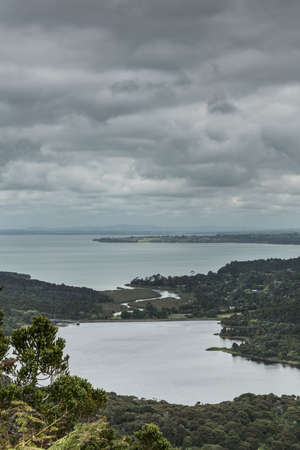 Auckland, New Zealand - March 2, 2017: Nihotupu Reservoir with off stream to the Big Bay under heavy dark gray skies. Forest around lake, Lots of gray water. LIne by dam.のeditorial素材