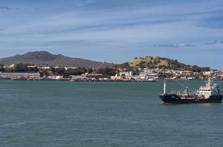 Auckland, New Zealand - March 6, 2017: Tanker sails in harbor in front of Devonport city under blue sky on green water. Rangitoto and Victoria volcanoes in background.のeditorial素材