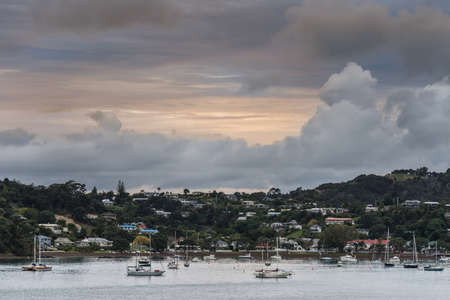 Bay of Islands, New Zealand - March 7, 2017: A major cyclone is building up over Paihia town set on a forested hill at the bay of the Pacific Ocean. Several pleasure boats on the water.のeditorial素材