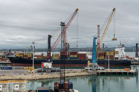 Napier, New Zealand - March 9, 2017: Penelope container ship unloads in the commercial port under heavy skies. Piles of containers, cranes and other harbor installations.のeditorial素材