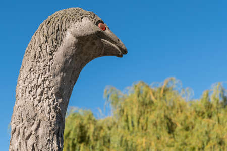 Queenstown, New Zealand - March 15, 2017: closeup of head of the extinct flightless bird Moa against blue sky and some green trees in background. Brown statue with red eyes.のeditorial素材