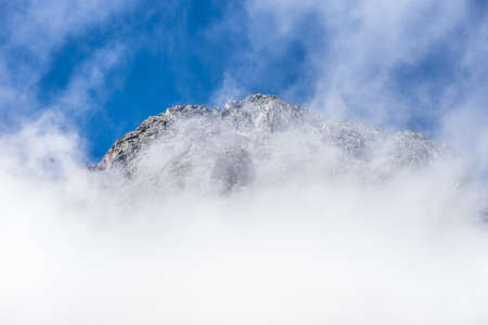 Fiordland National Park, New Zealand - March 16, 2017: Tall snow covered mountain peaks through white clouds near Monkey Creek valley under blue sky.の写真素材