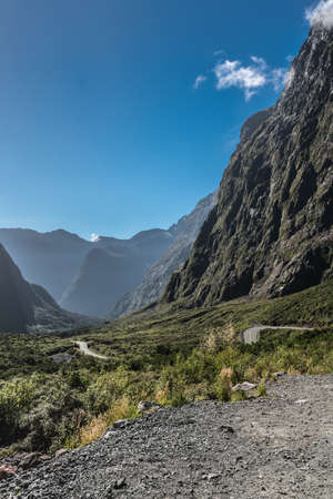 Fiordland National Park, New Zealand - March 16, 2017: Mountain range and road down under Hommer Tunnel under blue sky. Sparse green non-tree vegetation.のeditorial素材