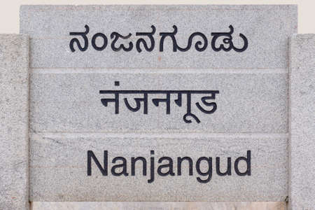 Nanjangud, India - October 26, 2013: Gray stone sign at entrance of the city showing its name in Hindi, Kannada and English languages.のeditorial素材