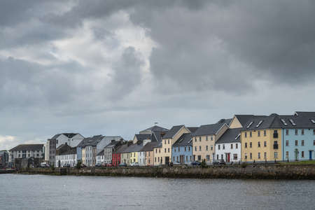 Galway, Ireland - August 3, 2017: Closeup of part of The Long Walk Quay of the old port seen from across the dark Corrib River mouth. All under heavy storm sky. The different paint colors of the houses shine.のeditorial素材