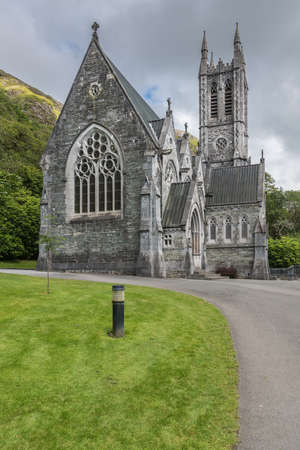 Connemara, Ireland - August 4, 2017: Closeup of the small gray Neo-Gothic church on the grounds of Kylemore Abbey against rocky green hills and under silver sky. Seen from the nave side.のeditorial素材