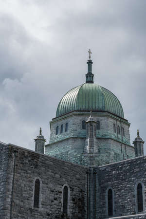 Galway, Ireland - August 5, 2017: Outside view of green dome with cross of the Cathedral under dark skies. Gray stone walls of the church.のeditorial素材