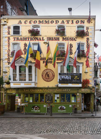 Dublin, Ireland - August 7, 2017: Historic Oliver St. John Gogarty pub on the corner of Temple bar and Bedford Row has yellow facade and displays many flags and U2 poster. Street scene.のeditorial素材