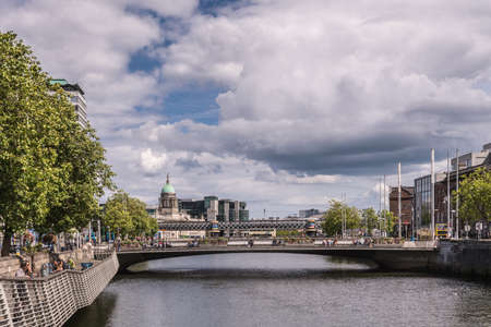 Dublin, Ireland - August 7, 2017: Looking east off O-Connell Bridge over Liffey River. Facades along the water, people over bridge, heavy cloudscape, some green trees and dome of the Custom House.のeditorial素材