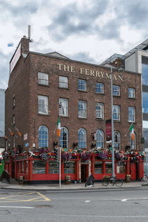 Dublin, Ireland - August 7, 2017: The historic brick Ferryman pub on the corner of Cardiff Lane and Sir John Rogerson's Quay along Liffey River in the old port. Red framed windows, flowers and flags. Street scene.のeditorial素材