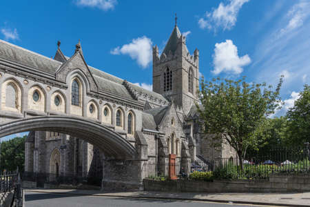 Dublin, Ireland - August 7, 2017: Gray stone Christ Church Cathedral with overpass link to Dublinia building against blue sky with white clouds. Green vegetation. Art market in back.のeditorial素材