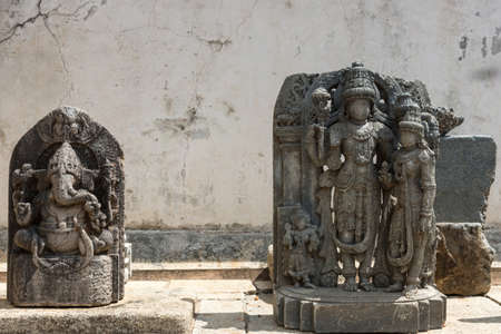 Mysore, India - October 27, 2013: Unearthed gray stone statues on display on the grounds of the Chennakesava Temple in Somanathpur. Set against  filthy white wall showing Nandi and Vishnu with consortのeditorial素材