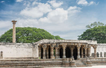 Mysore, India - October 27, 2013: Seen from inside temple grounds, looking at the entrance to the domain with the Vijaya Lamp Pole sticking out above the wall. Blue sky with white clouds. Top of green trees.のeditorial素材