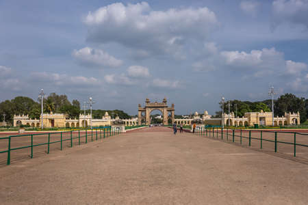 Mysore, India - October 27, 2013: Brown stone main East Gate to Mysore Palace with entire yellow side buIldings under cloudscape. Visitors add colors.のeditorial素材