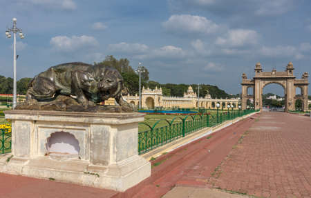 Mysore, India - October 27, 2013: Combination of brown East gate and dark brown bronze statue of aggressive lioness in front garden of Mysore Palace under cloudscape.のeditorial素材