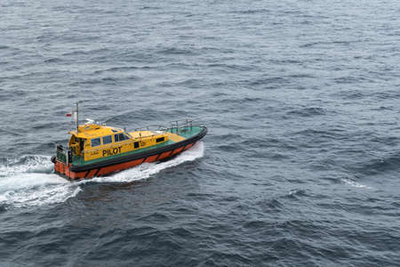 Tasman Sea, Australia - March 21, 2017: Focus on yellow Pilot boat leaving ship while creating white water trail.  No sky, only water and the boat in photo.のeditorial素材